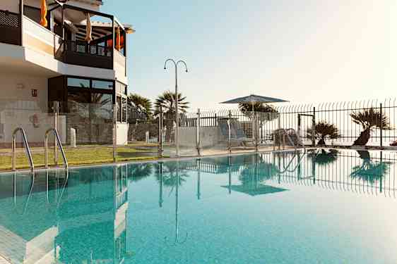 Uima-allas, jota ympäröi lasi-aita, näkymä nurmikolle ja aurinkotuoleille varjon alla. (Tekoälyn luoma teksti)