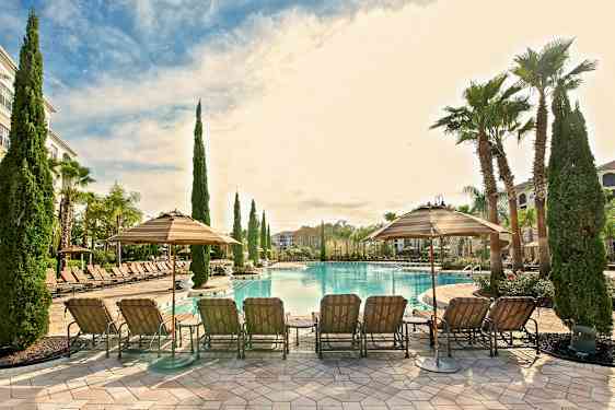 Ulkouima-allas, jossa aurinkotuoleja ja varjoja viihtyisässä ympäristössä, jossa on palmuja ja hyvin hoidettuja alueita. (Tekoälyn luoma teksti)