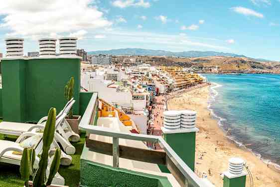 Näköala kattoterassilta aurinkotuoleilla kohti rantaa ja kaupunkimaisemaa. (Tekoälyn luoma teksti)