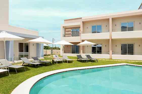 Uima-allas-alue aurinkotuoleilla ja aurinkovarjoilla vaaleiden rakennusten edessä. (Tekoälyn luoma teksti)