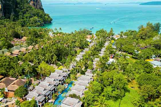 Ilmakuva trooppiselta alueelta, jossa on palmuja, rakennuksia ja uima-allas, taustalla meri. (Tekoälyn luoma teksti)