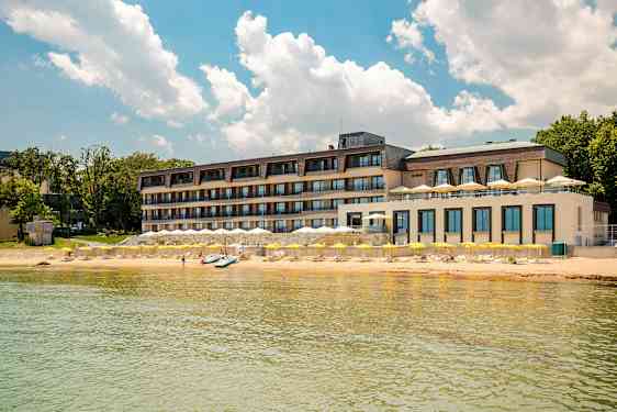 Monikerroksinen hotelli rannalla keltaisten aurinkovarjojen ja kirkkaansinisen taivaan alla. (Tekoälyn luoma teksti)