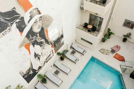 Kuva uima-altaasta, jota ympäröivät aurinkotuolit ja säkkituolit, ja jossa on suuri seinämaalaus. (Tekoälyn luoma teksti)