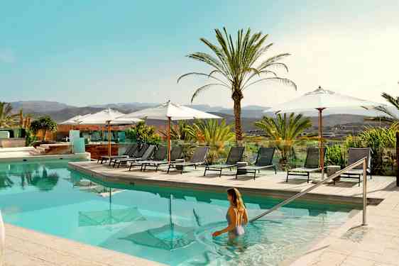 Uima-allasalue aurinkotuoleineen ja varjoineen, ympärillä palmuja ja näkymä maisemaan. (Tekoälyn luoma teksti)