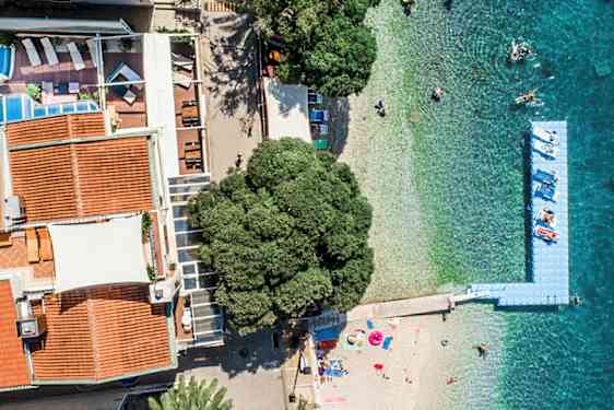 Ilmakuva rakennuksista, joissa on punaiset katot, uima-allas, ranta ja turkoosinsininen meri. (Tekoälyn luoma teksti)