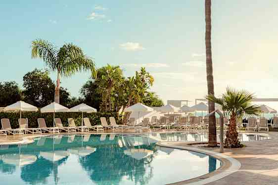 Ulkoallas, jonka ympärillä aurinkotuoleja, aurinkovarjoja ja palmuja. (Tekoälyn luoma teksti)