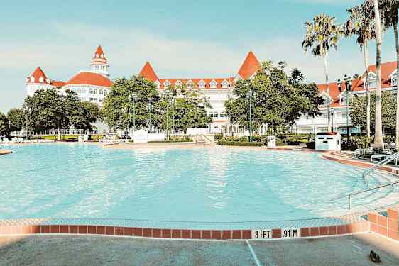 Kuva uima-altaasta, jonka taustalla on tyylikäs valkoinen hotelli ja punaiset katot. (Tekoälyn luoma teksti)