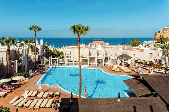 Näkymä hotellialueelle, jossa on uima-allas ja aurinkotuoleja, meri näkyy taustalla. (Tekoälyn luoma teksti)