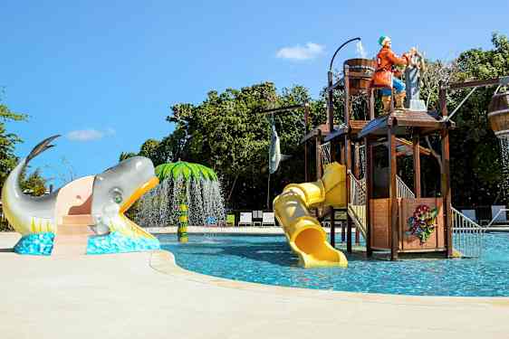 Lasten uima-allas, jossa vesiliukumäkiä, merirosvoteema ja hahmoja, kuten valas ja palmu. (Tekoälyn luoma teksti)