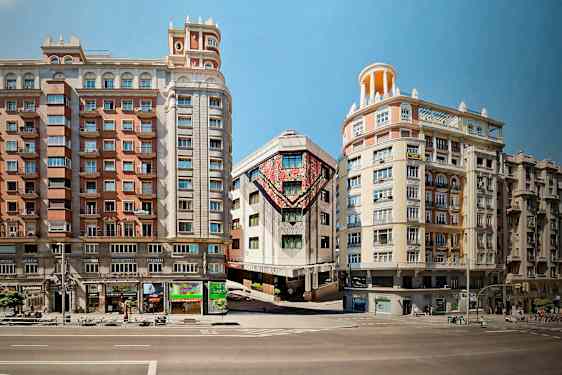 Kolme rakennusta sijaitsee kadun varrella, ja keskimmäisen rakennuksen julkisivulla on värikkäitä taideteoksia. (Tekoälyn luoma teksti)