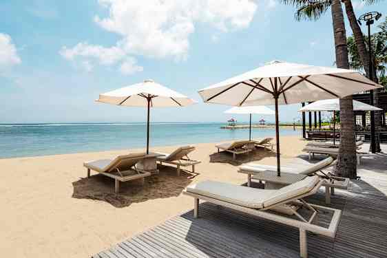 Ranta, jossa aurinkotuoleja ja varjoja kirkkaan sinisen meren äärellä. (Tekoälyn luoma teksti)