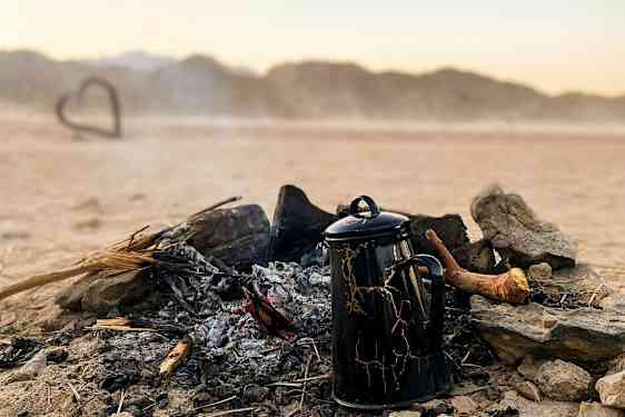 Kahvikannu seisoo sammuneen nuotion vieressä autiomaan maisemassa. (Tekoälyn luoma teksti)