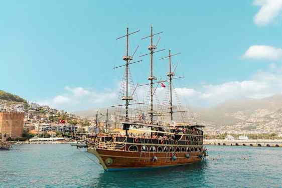 Suuri purjealus on satamassa kaupungin ja vihreiden kukkuloiden edustalla. (Tekoälyn luoma teksti)