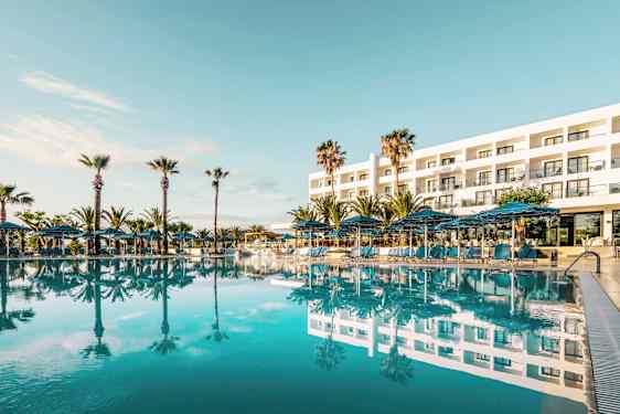 Hotellin ulkopuoli, jossa suuri uima-allas edessä ja ympäröivät palmut. (Tekoälyn luoma teksti)