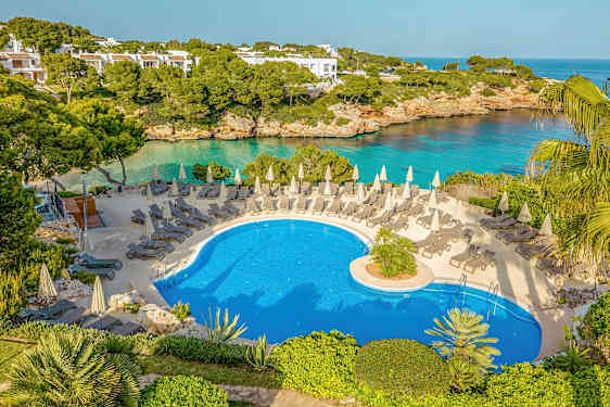 Ulkoallas, jossa aurinkotuoleja ja varjoja, ympäröitynä vehreydellä ja näkymällä merelle. (Tekoälyn luoma teksti)