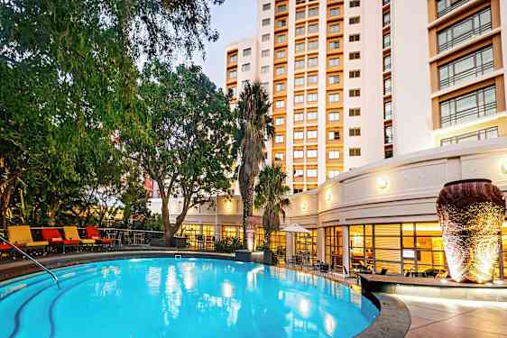 Valaistu ulkouima-allas, jota ympäröivät vihreät kasvit ja taustalla oleva rakennus. (Tekoälyn luoma teksti)