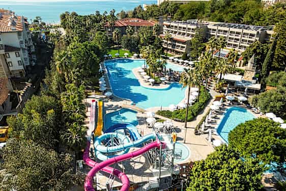 Näkymä lomakeskuksesta, jossa on useita uima-altaita ja vesiliukumäkiä, vihreyden ympäröimänä. (Tekoälyn luoma teksti)