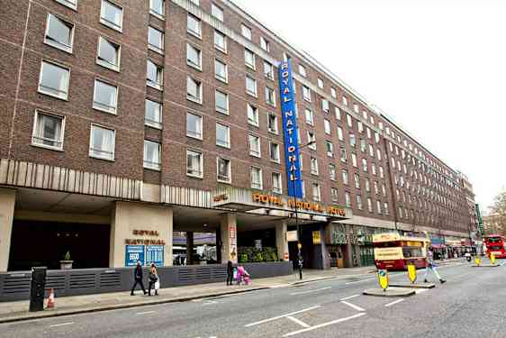 Kuva Royal National Hotellista kadulta, jossa näkyy useita busseja ja jalankulkijoita. (Tekoälyn luoma teksti)