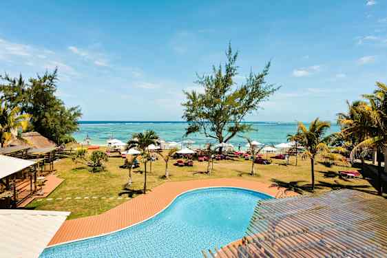 Uima-allas, jossa on turkoosia vettä, nurmikon, puiden, aurinkotuolien ja varjojen edessä rannan tuntumassa. (Tekoälyn luoma teksti)