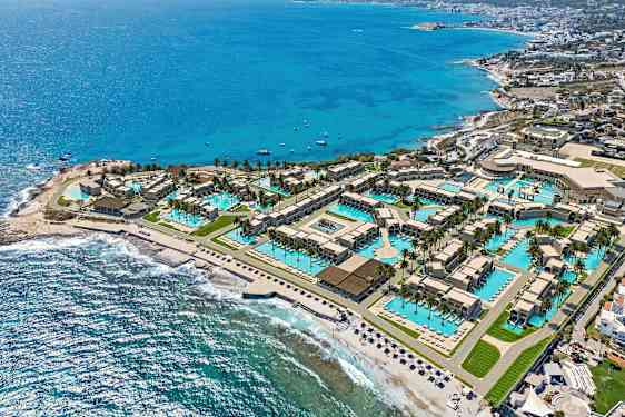 Ilmakuva lomakeskuksesta rannalla, jossa on uima-altaita, rakennuksia ja ranta meren äärellä. (Tekoälyn luoma teksti)