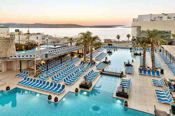 Suuri allasalue aurinkotuoleilla, palmuilla ja näköalalla merelle auringonlaskun aikaan. (Tekoälyn luoma teksti)