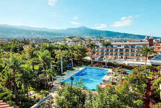 Uima-allas, jota ympäröivät kasvit ja rakennukset, taustalla vuori. (Tekoälyn luoma teksti)