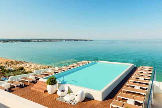 Kattoallas, jonka reunalla aurinkotuoleja, näkymä rannalle ja merelle. (Tekoälyn luoma teksti)