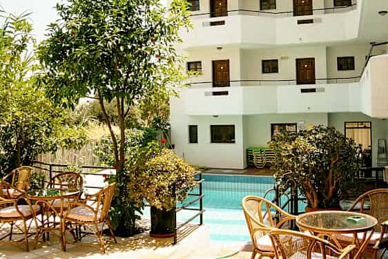 Ulkouima-allas, jota ympäröivät kasvillisuus ja istuimet, taustalla valkoinen rakennus parvekkeineen. (Tekoälyn luoma teksti)