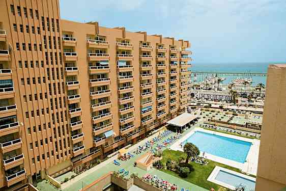 Korkea rakennus, jossa on parvekkeita, sekä uima-allas edessä ja venesatama taustalla. (Tekoälyn luoma teksti)