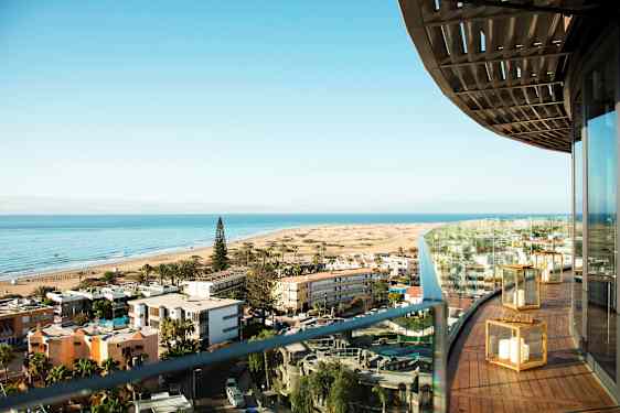 Näkymä rannalle, jossa on rakennuksia ja metsää, nähtynä parvekkeelta. (Tekoälyn luoma teksti)