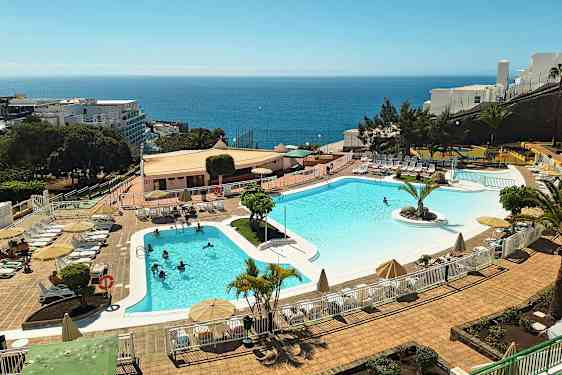 Ulkoallas lomahotellissa, jossa on aurinkotuoleja ja aurinkovarjoja. Meri näkyy taustalla. (Tekoälyn luoma teksti)