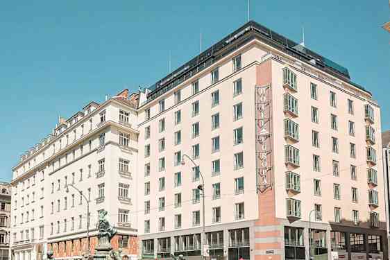 Kaupunkinäkymä, jossa on useita rakennuksia, mukaan lukien hotelli, jossa on kyltti "Hotel Europa", kirkkaan sinisen taivaan alla. (Tekoälyn luoma teksti)