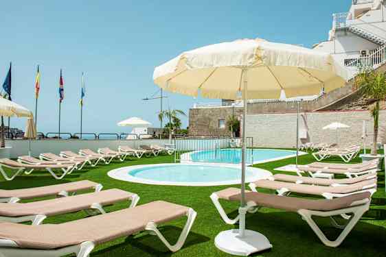 Ulkouima-allasalue, jossa on aurinkotuoleja ja aurinkovarjoja, vihreän nurmikon ympäröimänä. (Tekoälyn luoma teksti)