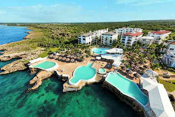 Ilmakuva lomakeskuksesta, jossa on uima-altaita ja varjokatteita meren äärellä. (Tekoälyn luoma teksti)