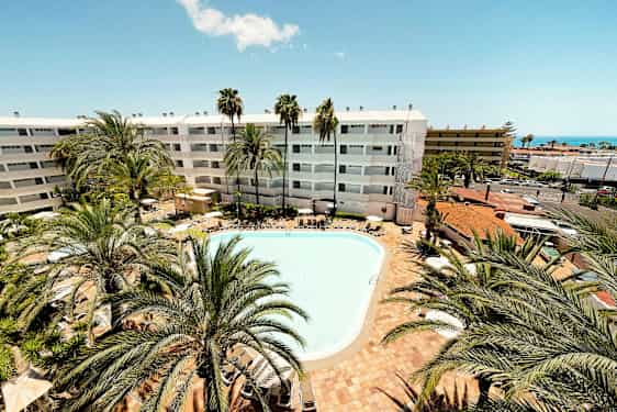 Ulkouima-allas, jota ympäröivät aurinkotuolit ja palmut. Taustalla näkyy hotellirakennus, jossa on valkoinen julkisivu. (Tekoälyn luoma teksti)