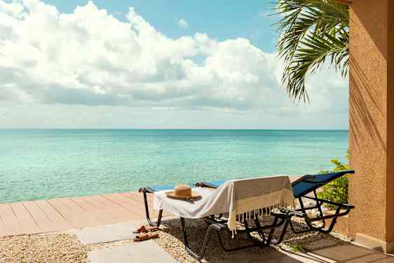 Kaksi aurinkotuolia, joissa on pyyhe ja hattu, seisovat matalan laiturin vieressä lähellä merta. Palmeoksa näkyy oikealla. (Tekoälyn luoma teksti)