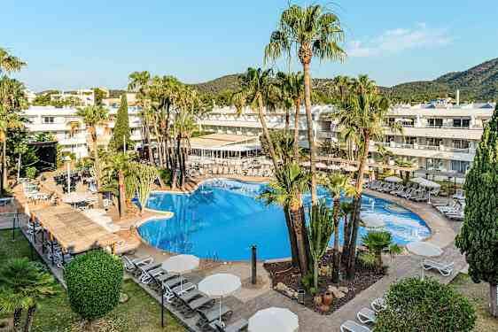 Hotellin uima-allas, jota ympäröivät aurinkotuolit ja aurinkovarjot, mukana palmuja ja rakennuksia taustalla. (Tekoälyn luoma teksti)