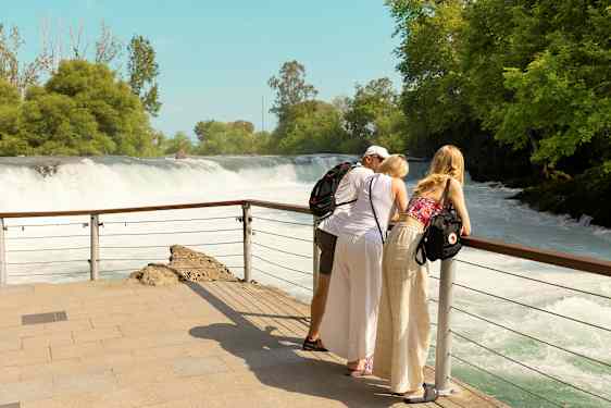 Kolme henkilöä nojaa kaiteeseen ja katsovat vesiputousta. (Tekoälyn luoma teksti)