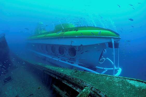 Vedenalainen näkymä sukellusveneestä vanhan laivanhylyn vieressä, ympärillä kaloja. (Tekoälyn luoma teksti)