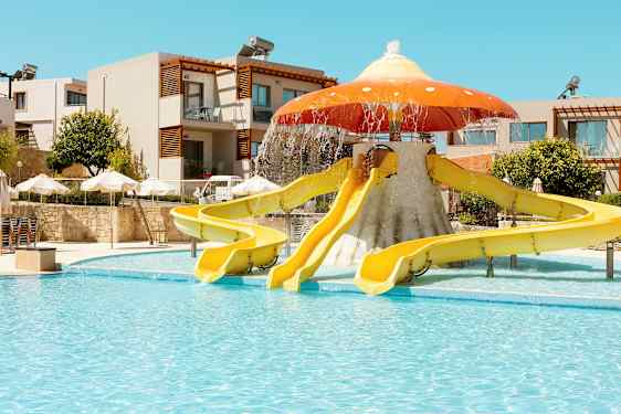 Ulkouima-altaan vieressä sienen muotoisia vesiliukumäkiä; taustalla rakennuksia ja aurinkovarjoja. (Tekoälyn luoma teksti)