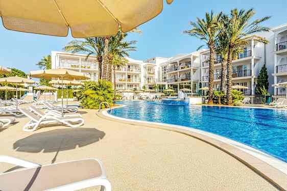 Ulkoallas, jota ympäröivät aurinkotuolit ja päivänvarjot, taustalla hotellirakennuksia. (Tekoälyn luoma teksti)