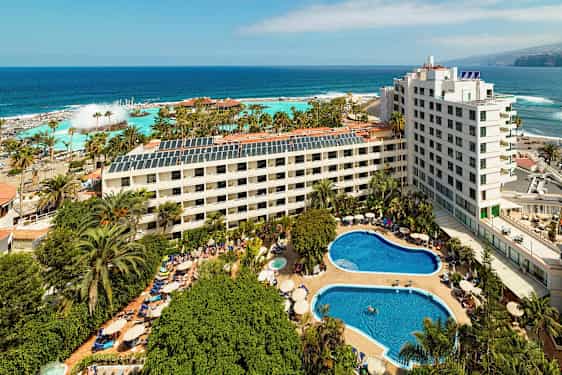 Hotellikompleksi, jossa on uima-altaita ja vehreyttä lähellä merta. (Tekoälyn luoma teksti)