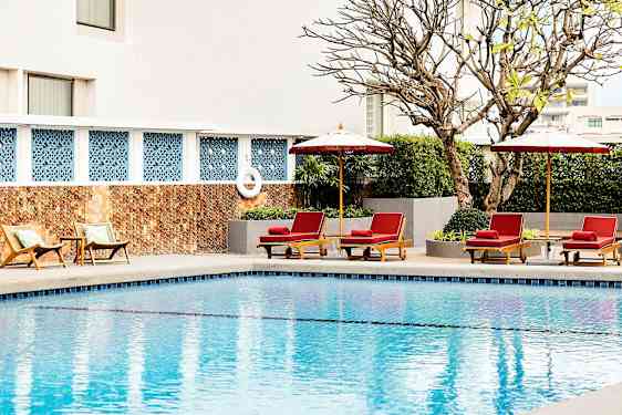 Uima-allas, jonka reunalla on aurinkotuoleja ja päivänvarjoja, ympärillä kasveja ja taustalla rakennuksen seinä. (Tekoälyn luoma teksti)