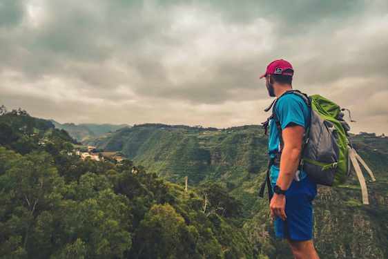 Reppu selässään oleva henkilö katselee vihreää laaksoa pilvisellä säällä. (Tekoälyn luoma teksti)