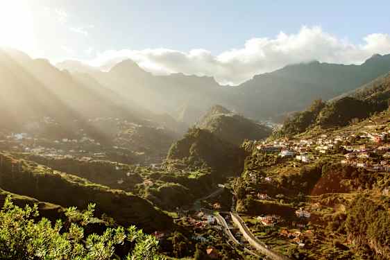 Näkymä vihreään laaksoon, jossa taloja ja vuoria taustalla aurinkoisena päivänä. (Tekoälyn luoma teksti)