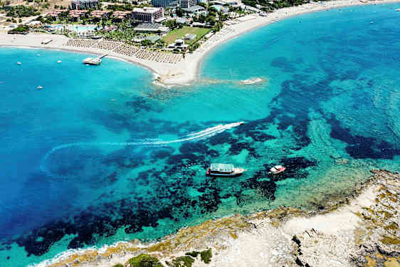 Ilmakuva hiekkarannasta turistialueella, jossa kirkasta sinistä vettä. (Tekoälyn luoma teksti)