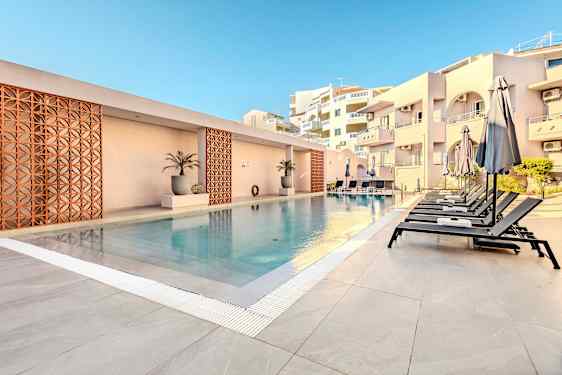 Ulkouima-allas, jonka vieressä on aurinkotuoleja ja varjoja, rakennusten ympäröimä. (Tekoälyn luoma teksti)