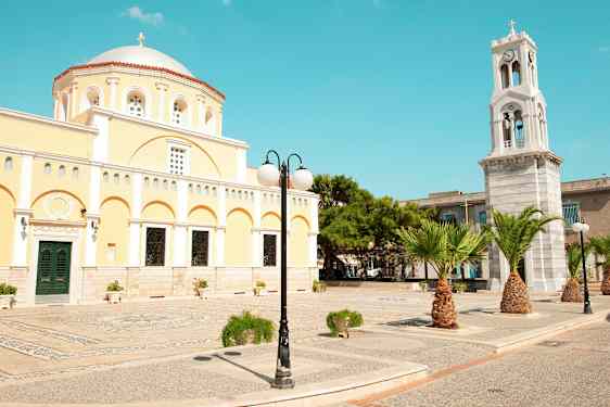Keltainen rakennus, jossa on kupoli ja kellotorni, sekä palmuja ja katuvalaisin. (Tekoälyn luoma teksti)