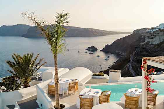 Ulkoterassi merinäköalalla ja kallioisella rannikkolinjalla, jota ympäröi valkoinen arkkitehtuuri ja kasvit. (Tekoälyn luoma teksti)