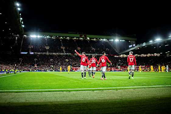 Jalkapalloilijat punaisissa paidoissa valaistulla jalkapalloareenalla iltapelissä. (Tekoälyn luoma teksti)